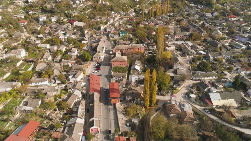 Top view of city in foothills of hills. Shot. Houses, roads and streets located on slopes of hills. Colourful old town is located in secluded area surrounded by mountains