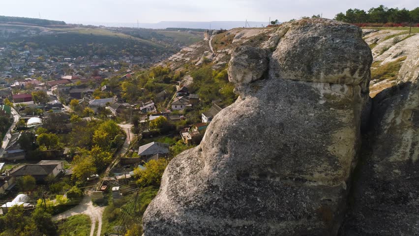 Top view of stone cliffs hanging on town. Shot. Houses located in valley surrounded by hills with rocky cliffs. Danger of living near rock cliffs