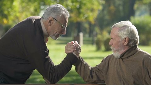 Positive senior men arm-wrestling outside, aged friends having fun together