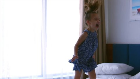 Happy little Caucasian girl jumping on the bed. Slow motion.
