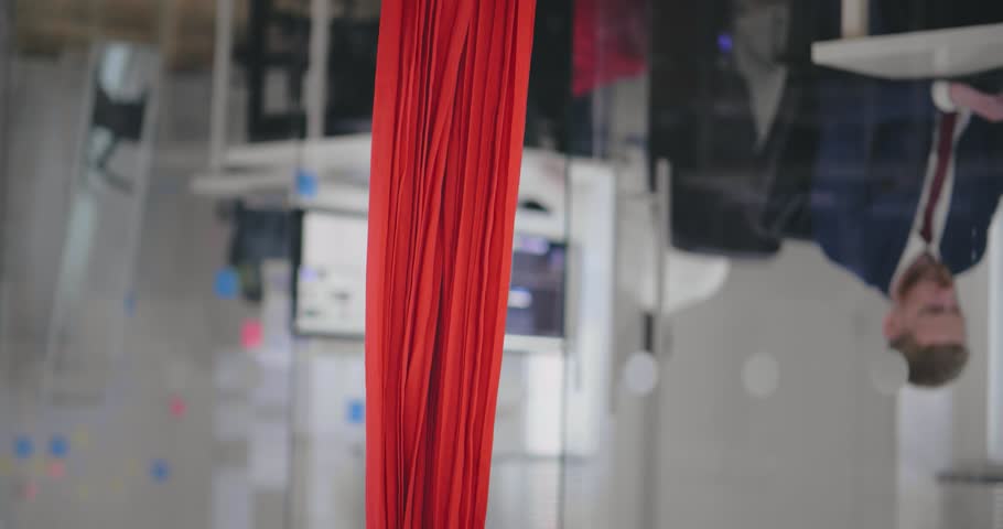 Woman holding coffee hanging upside down in yoga hammock, the coffee is spilled. Parallel reality, different worldview concept