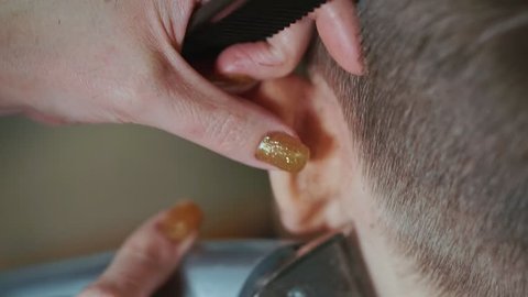 Close-up of the hand of a woman hairdresser with a hair cutting machine making a hair edging boy. She makes him a modern haircut.