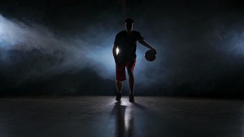one young adult man, basketball player dribble ball, dark indoors basketball court slow motion
