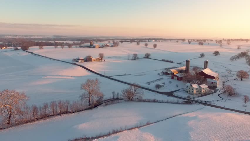 Aerial flight to red farmhouse over snow-covered fields and beyond Amish country Lancaster Pennsylvania Concept: winter, holidays, cold, snow traditional, nostalgic