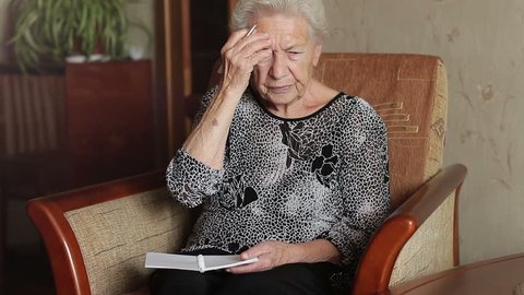 Old man's memory loss. An old woman trying to remember something and write in a notebook