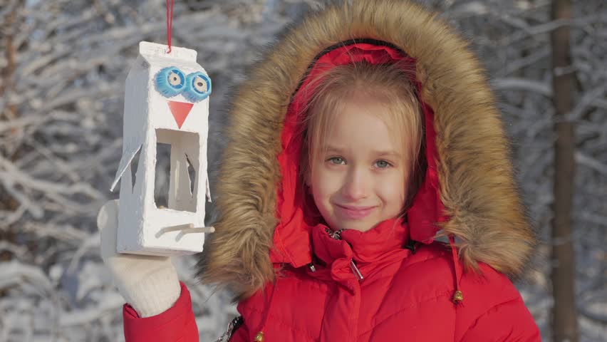 Pretty cute girl at winter park with bird feeder. Bird feeder on tree, winter vacation and holidays concept, children outdoor activities.