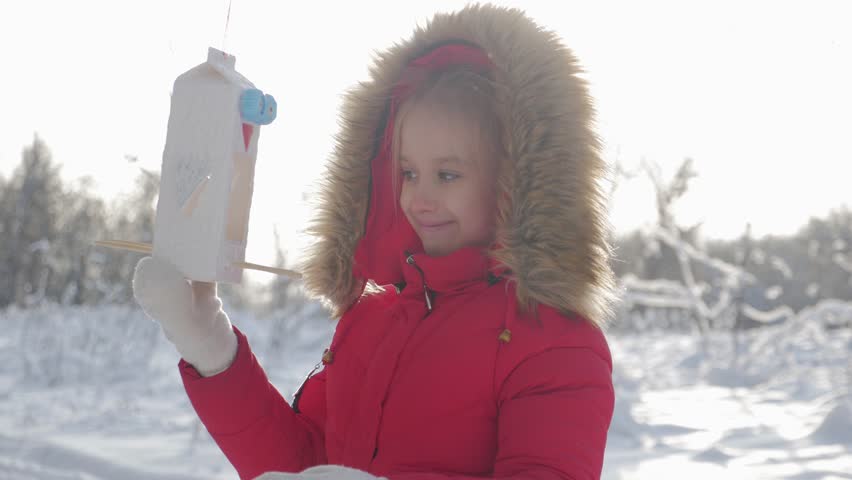 Pretty cute girl at winter park with bird feeder. Bird feeder on tree, winter vacation and holidays concept, children outdoor activities.