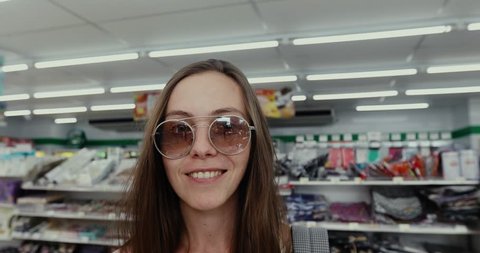 Portrait, young woman in sunglasses looking at camera and smiles while in produce section in supermarket 