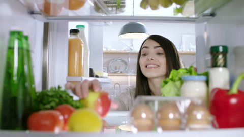 Woman opens refrigerator full of healthy food and takes an apple. POV from inside the refrigerator.