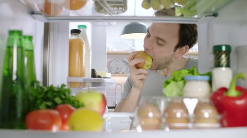 A man opening a fridge looking for a healthy snack takes an apple. POV from inside the refrigerator.