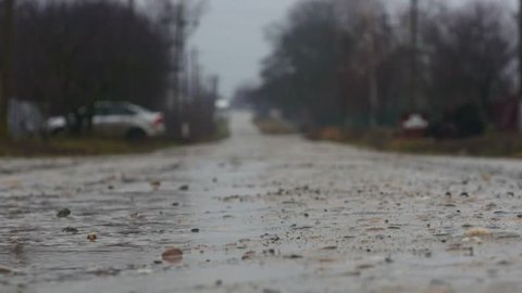 Man runs for cover through gravel driveway on rainy day, while car drives on wet road in background.