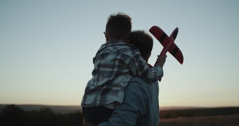 Closeup hugging dad with his son, and holding a big airplane watching sunset.