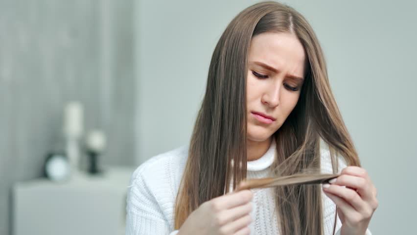 Upset young Caucasian woman looking on weak unhealthy dry hair ends at home interior Royalty-Free Stock Footage #1021398304