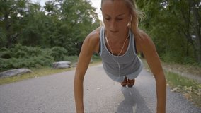 Sportive young woman exercising outdoors, strength training push ups after jogging. People body conscious and heathy lifestyle concept. Slow motion