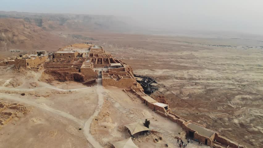 Masada - Aerial footage of the ancient fortification in the Southern District of Israel. Moving forward. Flying around Masada. The view from the top. Tourists walk among the ruins. 4k Royalty-Free Stock Footage #1021402363