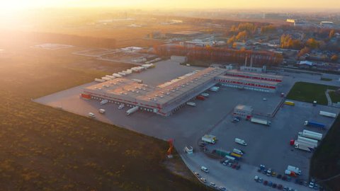 Aerial view of logistics center with warehouse, loading hub with many semi-trailers truck load/unload goods at sunset