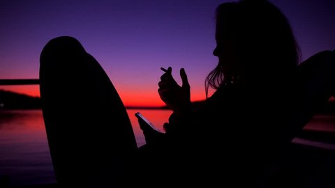 Silhouette of Young Unidentified Woman Smoking Weed Joint or Cigatette Againts Amazing Beach Sunset near Water. 4K Slowmotion.