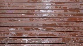 A video of light rain on a wet wooden deck reflecting the sky.