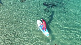 Aerial drone video of fit man dressed as Santa Claus practising SUP or Stand Up Paddle in tropical turquoise sea