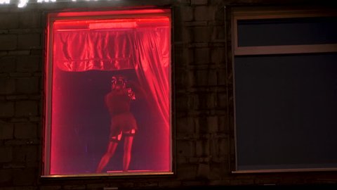 On the street of Amsterdam's red-light district, a woman in uniform dances a striptease. Easy erotic girls in the window with red neon. Striptease for men in a nightclub. Nightlife for adults 4k.