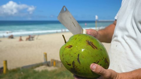 Man holding the chop knife to peeling and shelling a green fresh coconut on the beach, Rio de Janeiro