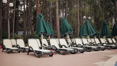 Rows of empty sun loungers stand in a wooded area at the pool.
