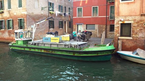 Venice, Italy-20 September, 2018: 4K Timelapse boat collecting rubbish by crane on canal. Workers gather trash and move goods by boat. Special boats with hoists taking out garbage, keep city clean-Dan