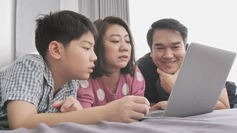 Happy family Father mother and son watching on laptop computer and having fun, Slow motion 4K  asian family rest on bed with laptop computer