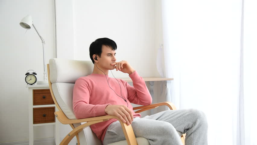 Portrait of a satisfied man relaxing with the arms in the head sitting on a chair at home with a warm light from a window. young man indoors with very handsome face in pink casual shirt | Shutterstock HD Video #1021436413