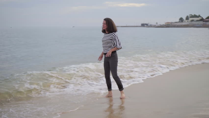 Beautiful middle aged woman jumping in seawaves. Happy barefoot woman having fun on seacoast. Hapiness concept