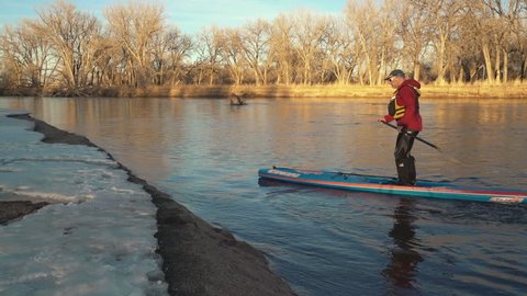 Kuner, CO, USA - February 4, 2017: Mature male paddler is paddling his racing stand up paddleboard by Starboard upstream of the South Platte River in a typical winter scenery.