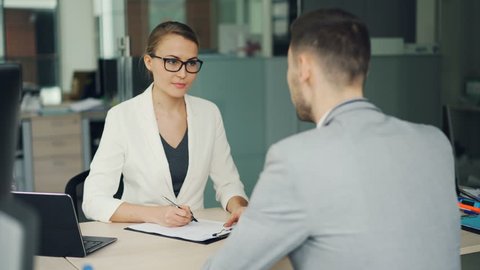 Pretty woman recruiter is talking to male candidate during job interviewer in office, girl is taking notes then shaking his hand and laughing. Success and workplace concept.