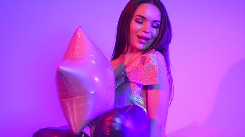 Beauty fashion model girl with heart shaped air balloons having fun, sitting on chair, laughing and spinning. Emotions. Holiday celebration. Beautiful young brunette woman on party. Slow motion 4K UHD