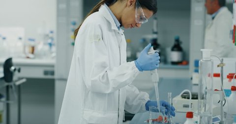 Portrait of female scientist with a pipette analyzes a liquid to extract the DNA and molecules in the test tubes in laboratory. Shot in 8K. Concept: research,biochemistry, pharmaceutical medicine