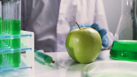 Bio scientist in gloves injects green solution or substance in genetically modified green apple in the laboratory
