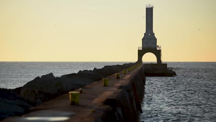 Birds fly, the lake michigan waters twinkle in the marina as the morning sunlight kisses the sea while the breakwater leads the way to the Port Washington Wisconsin lighthouse.