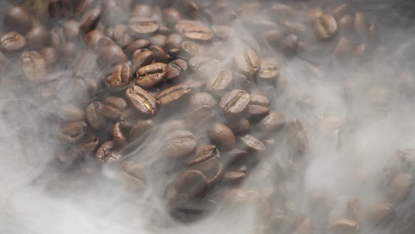 Fragrant coffee beans are roasted in a frying pan, smoke comes from coffee beans. The whole composition scrolls slowly around the camera. Scoop stir coffee beans. Royalty-Free Stock Footage #1021452235