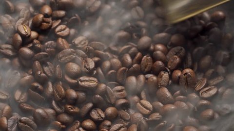 Fragrant coffee beans are roasted in a frying pan, smoke comes from coffee beans. The whole composition scrolls slowly around the camera. Scoop stir coffee beans.