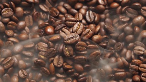 Fragrant coffee beans are roasted in a frying pan, smoke comes from coffee beans. The whole composition scrolls slowly around the camera. 