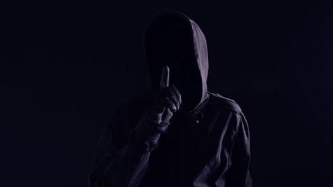 Hooded maniac with finger on lips gesturing shh sign to silence victim before attack, slow motion