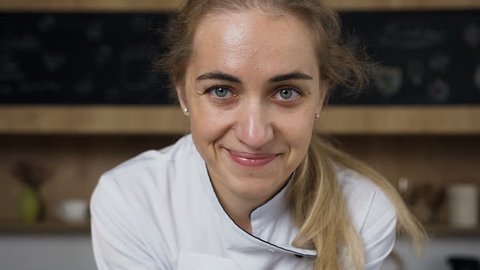Portrait shot of young smiling woman, female chef in white tunic with colorful macaroons in hands. Dolly shot. 