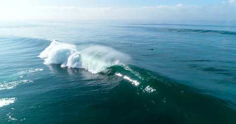 Slow motion aerial view of large blue ocean waves crashing on sunny day