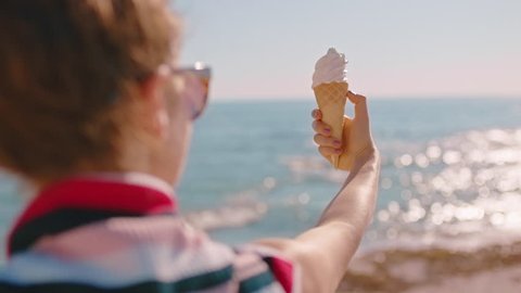 close up hand woman holding ice cream vanilla flavored dessert on beautiful sunny beach enjoying summer vacation eating soft serve