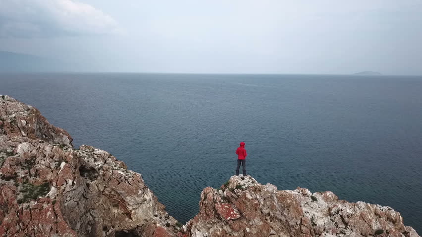A girl stands on the edge of a cliff above the sea. Aerial shooting from the drone. Lake Baikal.