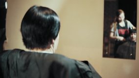 Mature woman having her hair cut at the hairdresser's. Girl hairdresser blows hairdryer trimmed hair from the female client, close-up view from the back.