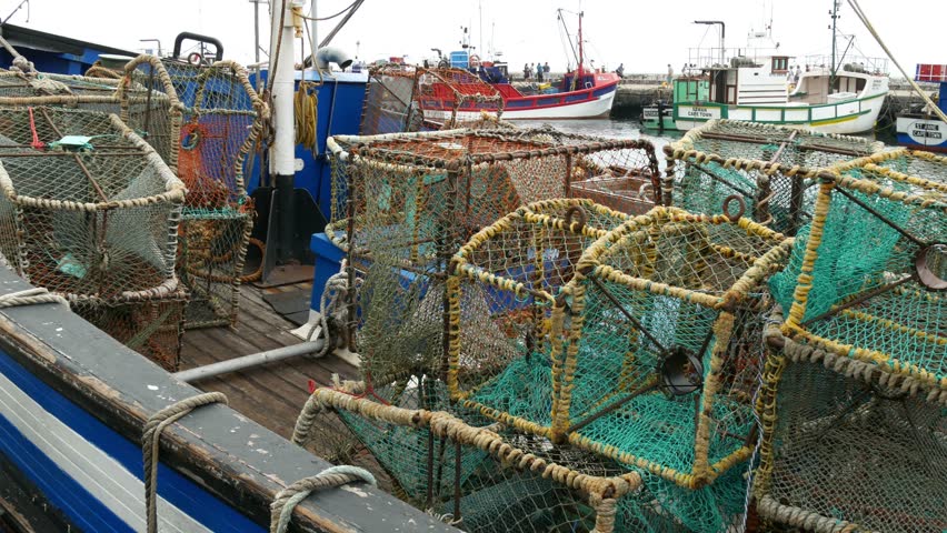 Pan of moored wooden fishing trawler full of square fishing nets with distant pier with other fishing boats & people to front of trawler with other moored boats at pier,  Kalk Bay, South Africa
