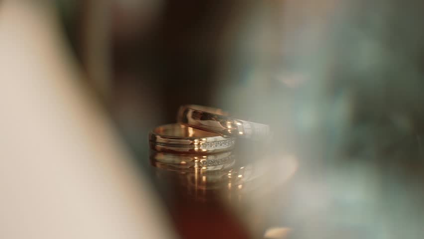 Two gold wedding rings lying on a table whit decorations shining with light close up macro. Transfusion of light on rings.. Close up Royalty-Free Stock Footage #1021486243