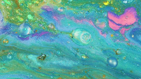 Colorful sparkling paints mix in beautiful patterns. Oil ink of blue, green, pink, yellow and other colors spread on the surface and mix one into another creating amazing textures and design.