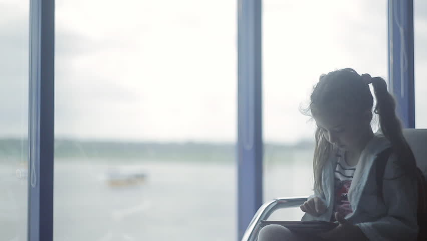 A little girl at the airport at the window uses a tablet | Shutterstock HD Video #1021489444