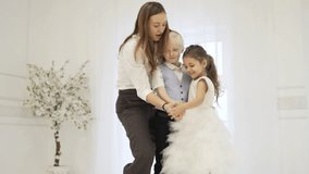 A woman funny teaches children to dance slow dance. Boy and girl hold hands, hug each other and laugh. Mom shows them in which direction to spin and runs away from the frame. Funny video